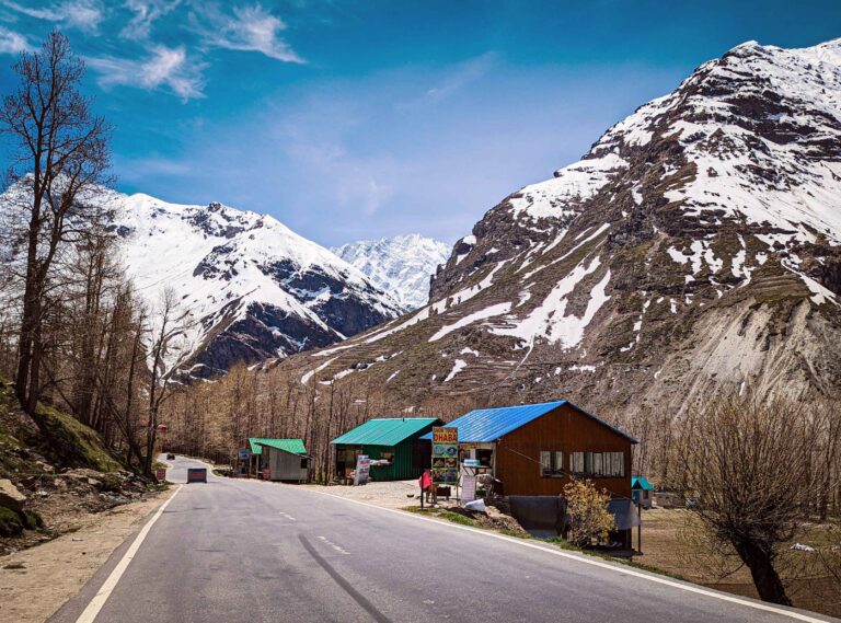 A desolate road leading to Sissu in Himachal Pradesh, flanked by rugged, barren landscapes and towering Himalayan peaks in the background, creating a striking contrast of solitude and grandeur.