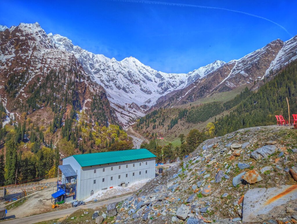 A breathtaking view of the serene mountain landscapes on the route from Manali to Lahaul, featuring the majestic Dhauladhar ranges, snow-capped peaks, lush valleys, and a winding road surrounded by natural beauty.