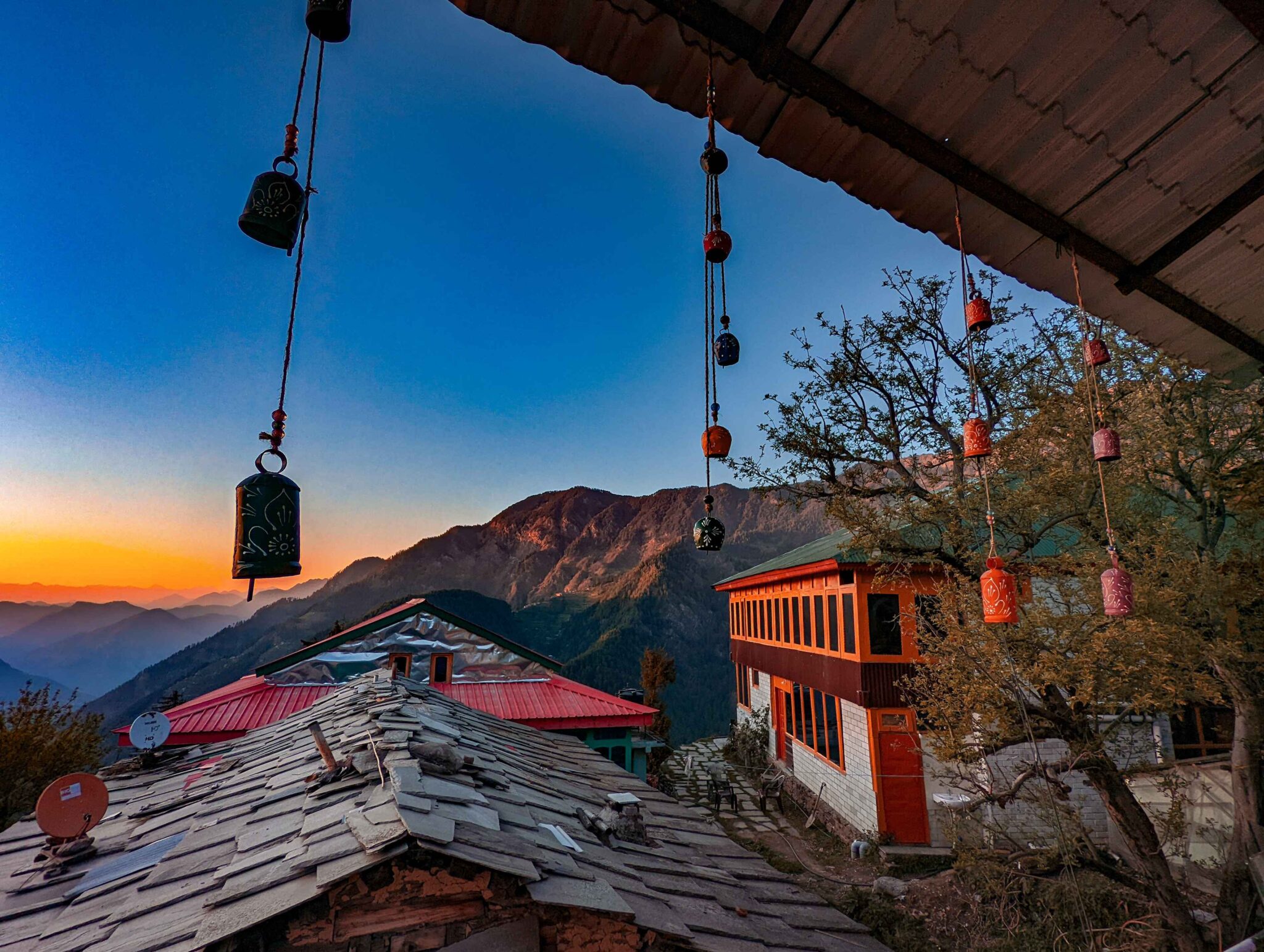 Stunning sunset over Shoja, Himachal Pradesh: Vibrant orange and pink skies casting a warm glow on the lush valleys, pine forests, and distant Himalayan peaks.