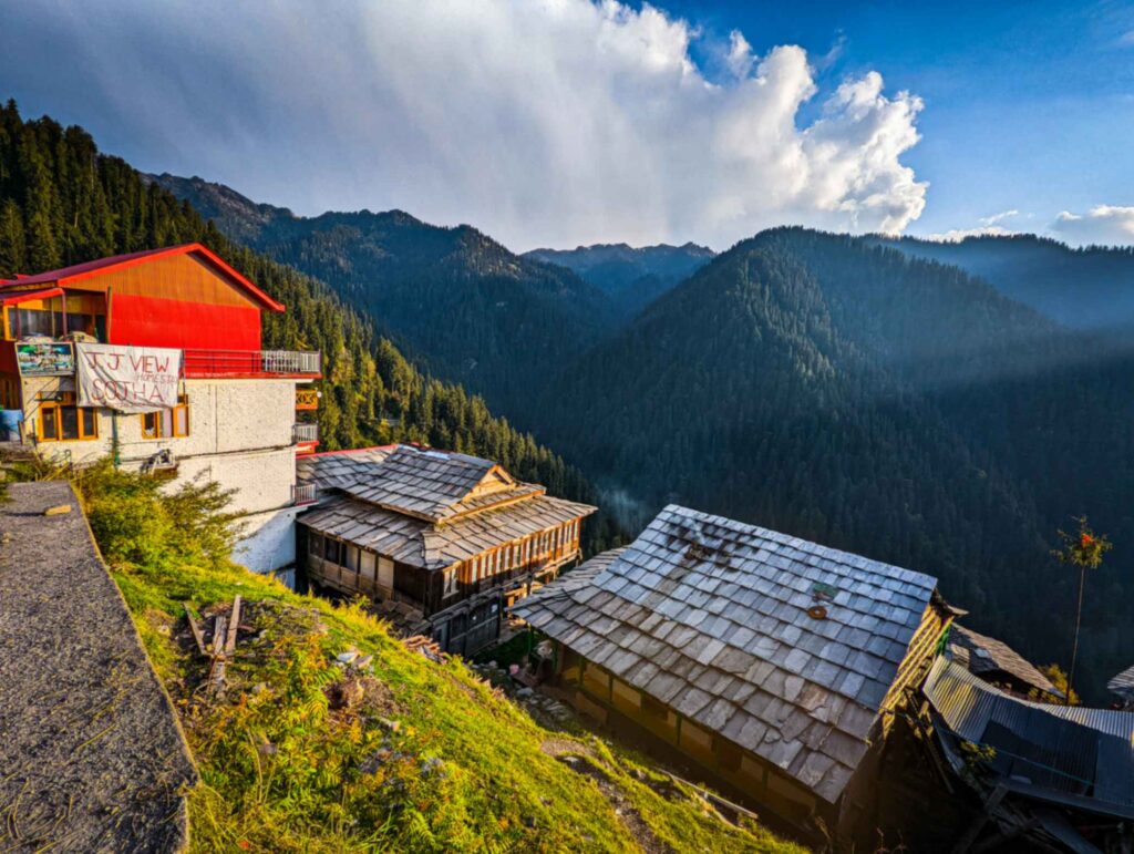 Tranquil landscape of Shoja, Himachal Pradesh, showcasing dense pine forests, rolling hills shrouded in mild sunlight, and a peaceful mountain village surrounded by natural beauty.