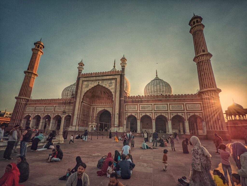 A bustling scene at the iconic Jama Masjid, featuring crowds of visitors gathered in its sprawling courtyard, highlighting the mosque's stunning domes, towering minarets, and timeless architectural beauty.