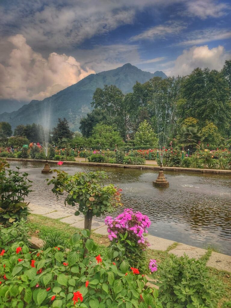 The iconic Mughal Garden in Srinagar, featuring meticulously landscaped terraces, vibrant flowerbeds, flowing fountains, and a backdrop of majestic mountains.