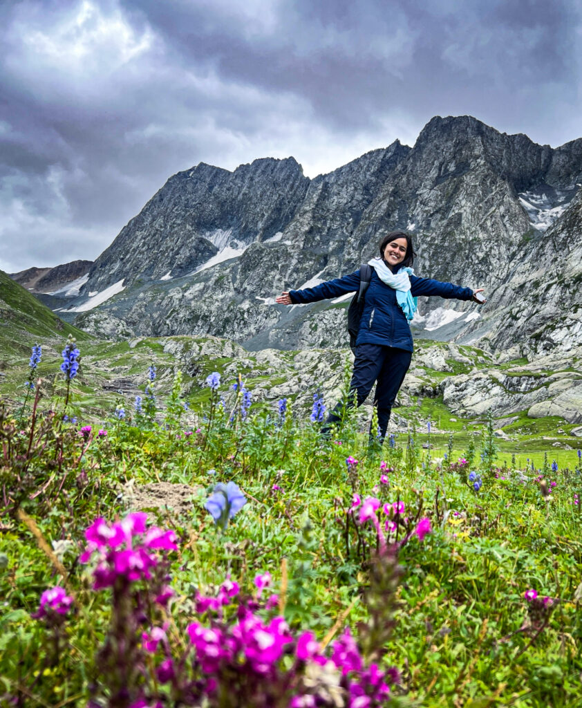 Standing amidst a lush field of Himalayan wildflowers on the Kashmir Great Lakes trek, surrounded by the grandeur of towering mountain ranges.