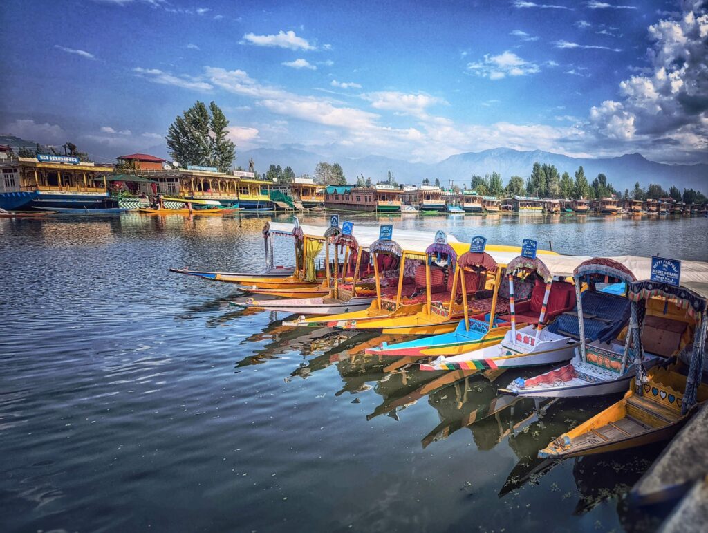 Tranquil Dal Lake featuring a colorful Shikara boats floating peacefully, with scenic mountains in the background.
