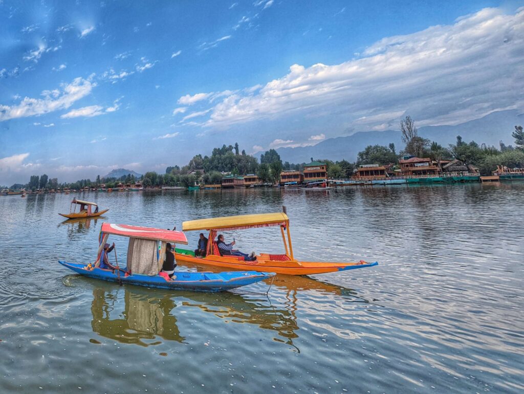 A picturesque view of Dal Lake, reflecting the surrounding mountains and vibrant Shikaras gliding across its calm waters.