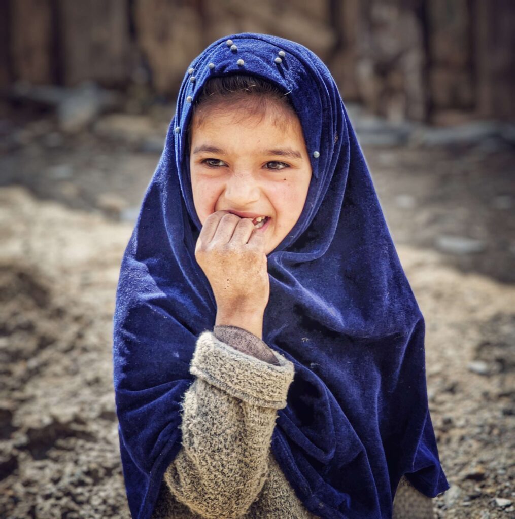 A smiling, shy Shina tribe girl child with sparkling eyes, adorned in traditional attire, capturing the warmth and innocence of her culture.