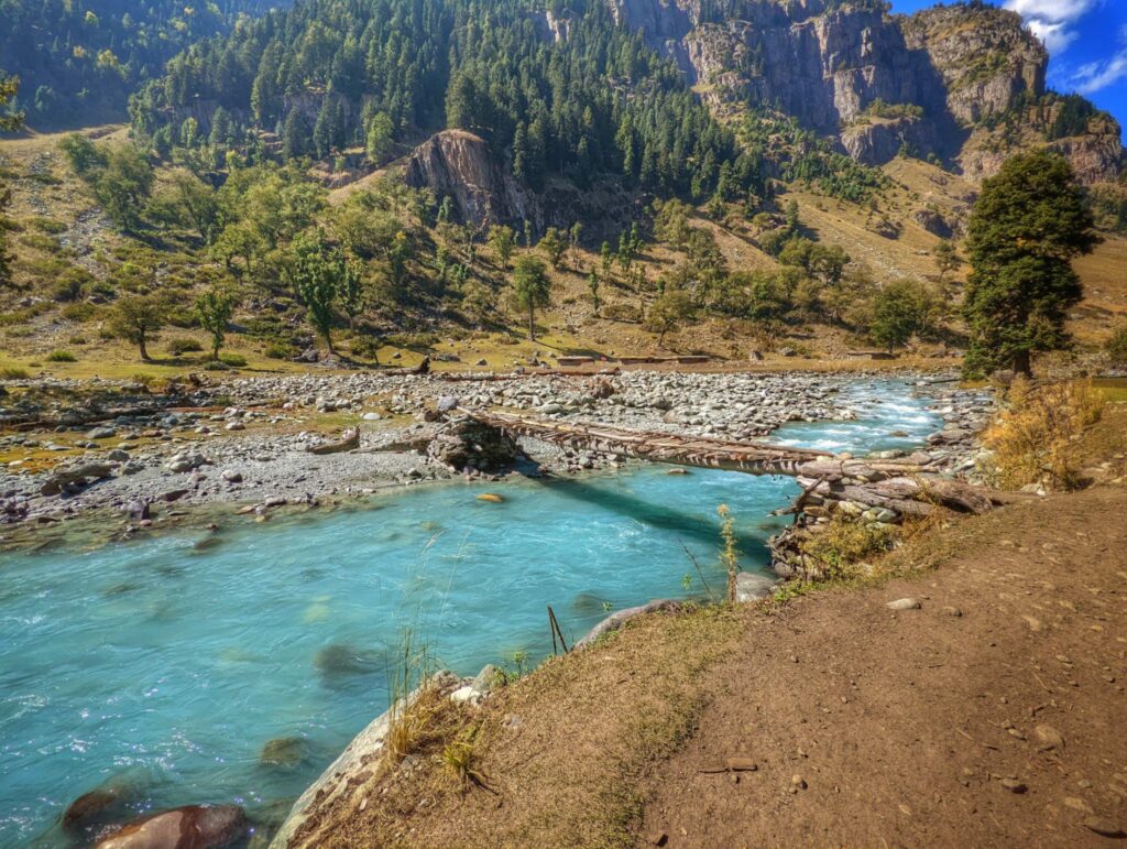 The crystal-clear Lidder River meandering through the picturesque Aru Valley in Kashmir, surrounded by lush meadows, dense forests, and towering Himalayan peaks.