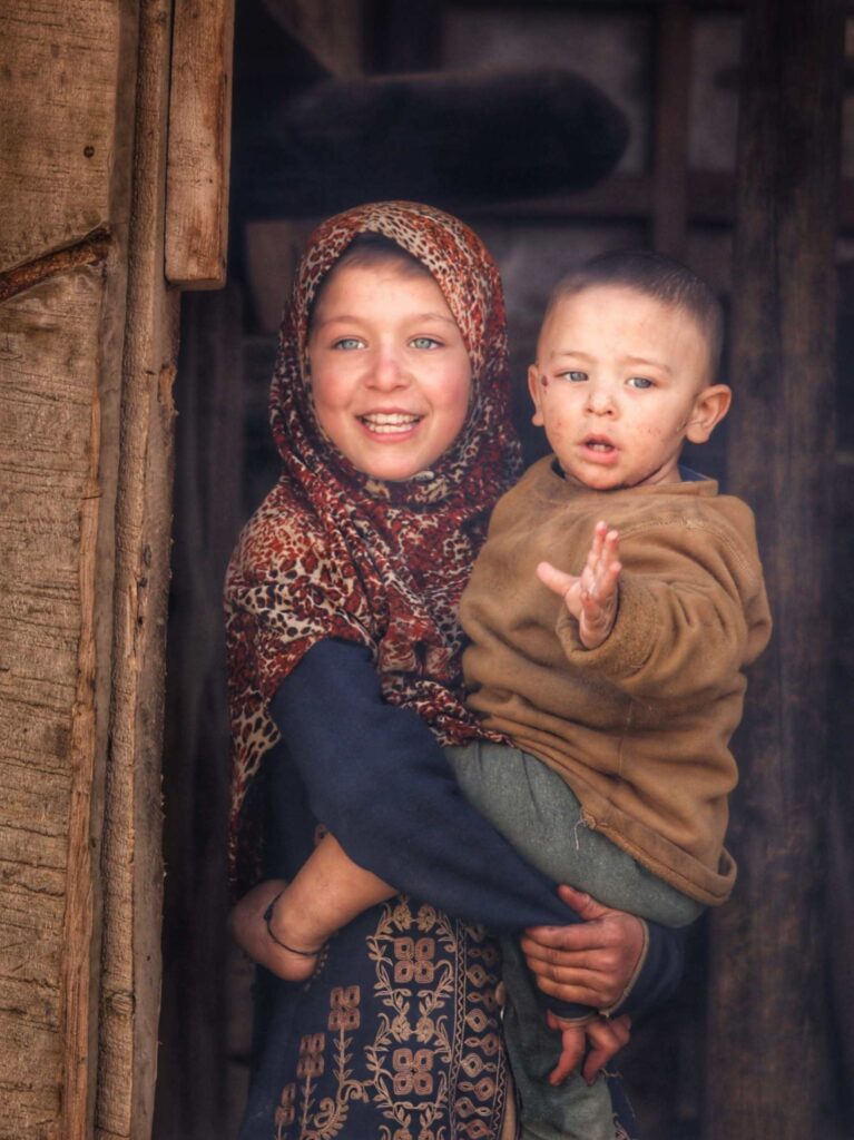 Shina tribe girl with pale eyes gently holding her baby brother in Tulail valley