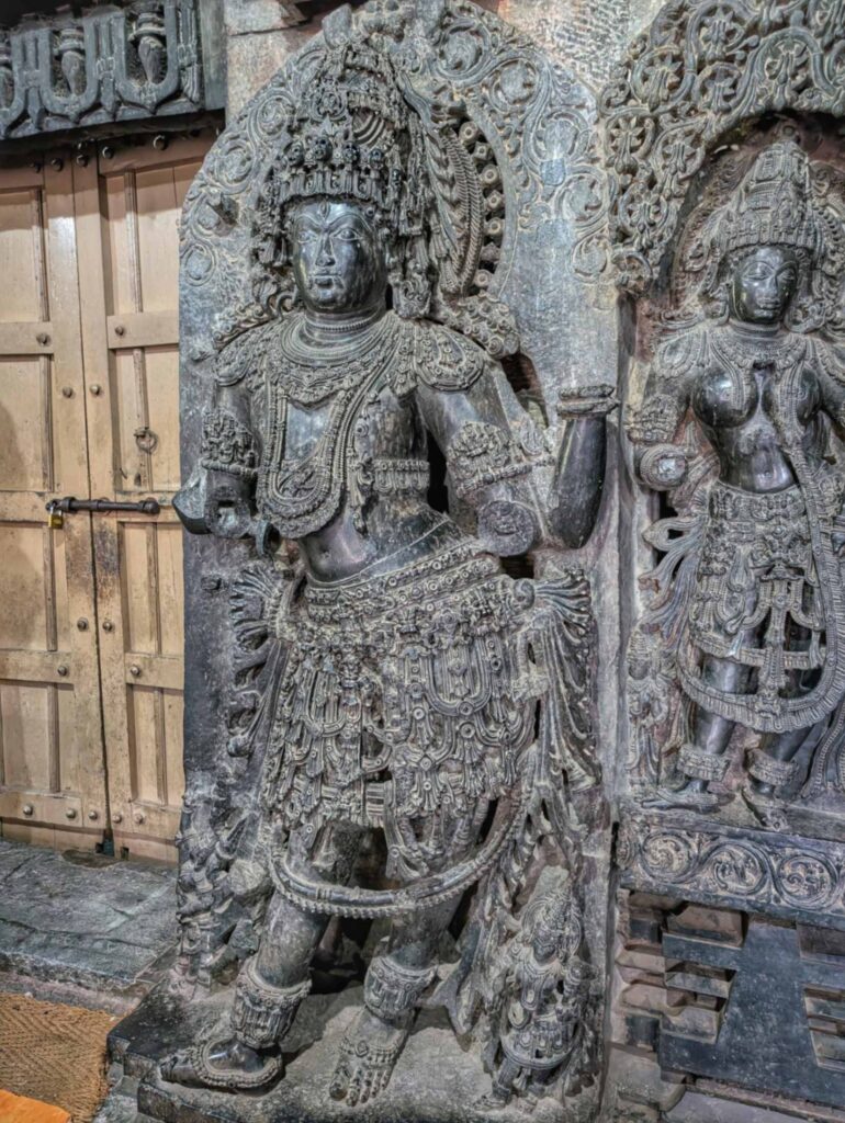 Stone sculpture of a fierce Hoysala temple gatekeeper standing guard at the temple entrance, adorned with detailed armor and ornate carvings typical of Hoysala architecture.
